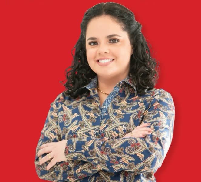 Professora Esther Moreira, sorrindo, de braços cruzados